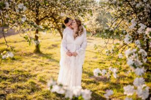 sesja ciążowa, zdjęcia we dwoje, sukienka boho, słoneczny dzień, plener, sad owocowy, kwiaty na drzewach, fotograf Koszalin, Barbara Rompska