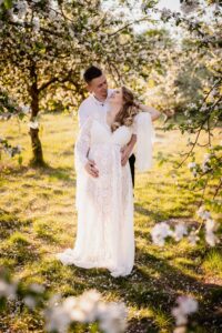 sesja ciążowa, zdjęcia we dwoje, sukienka boho, słoneczny dzień, plener, sad owocowy, kwiaty na drzewach, fotograf Koszalin, Barbara Rompska